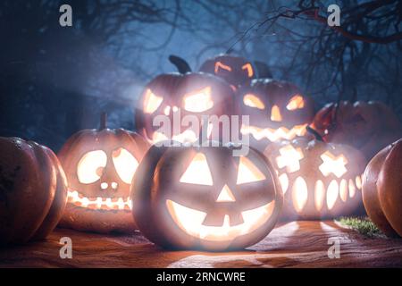 Spooky halloween background. Halloween Pumpkins In Spooky Forest At Night. Gloomy forest sunset with haunted evil glowing eyes of Jack O' Lanterns on Stock Photo