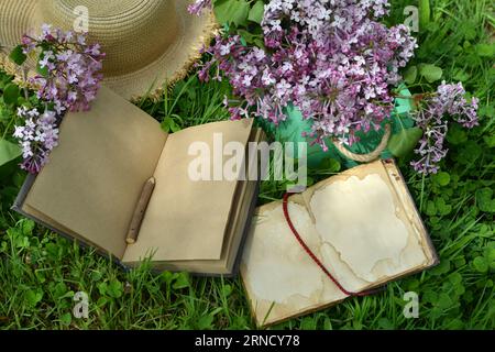 Vintage still life with open book or diary, hat and lilac flowers bouquet in the garden. Summer and spring season concept Stock Photo