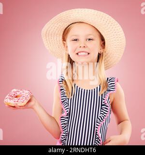 Happy, portrait and girl with a donut or child with sugar, dessert and sweet craving on pink background in studio. Face, smile and hungry kid with Stock Photo