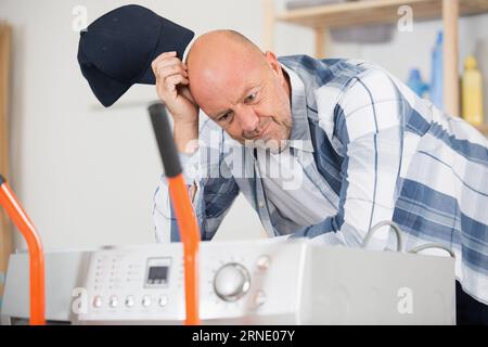 confused delivery man leaning on washing machine Stock Photo