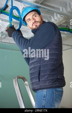 electrician on stepladder installs lighting to the ceiling in office Stock Photo