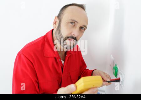 electrician a wall socket with electronic multimeter Stock Photo
