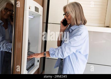 mature old woman talking on the phone and using an ATM Stock Photo