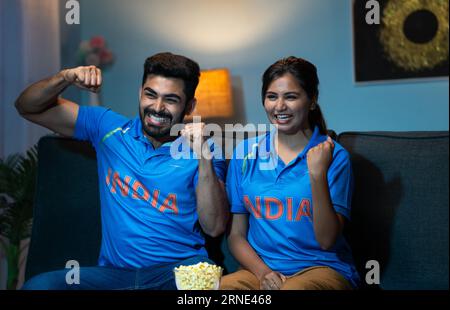 Indian couples celebrating indias win while watching live cricket sports match on tv or television at home - concept of Victory Celebration, Excited F Stock Photo