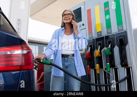 mature old woman refuels the car with a gas gun Stock Photo