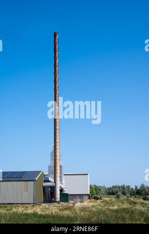 Millingen aan de Rijn, Gelderland, July 10 2023 - High industrial chimney against blue sky at the banks of the river Waal Stock Photo