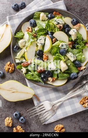 Delicious salad with blueberries, lettuce, gorgonzola cheese, walnuts and pear close-up in a plate on the table. Vertical top view from above Stock Photo