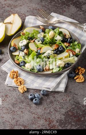Autumn salad consisting of ripe pears, blueberries, blue cheese, lettuce and walnuts close-up in a plate on the table. Vertical Stock Photo