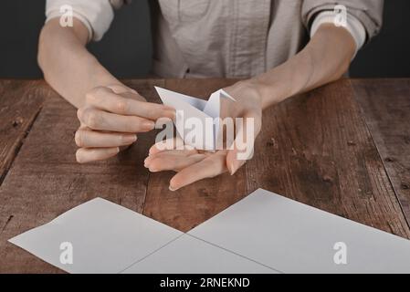 hands of an elderly woman fold origami paper. Creating an origami paper crane, close-up Stock Photo