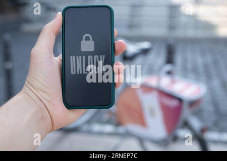 human hand unlock share bike on sidewalk next to street with phone to drive in city with bicycle Stock Photo
