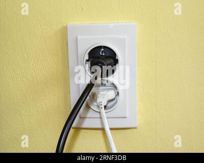 A black plug and a white plug in the socket Stock Photo