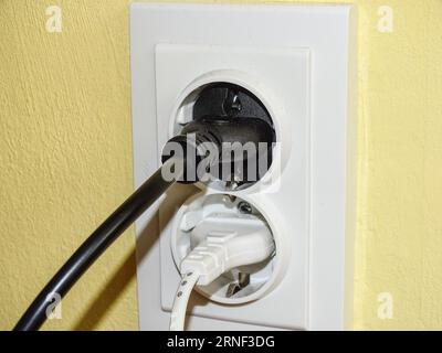 A black plug and a white plug in the socket Stock Photo