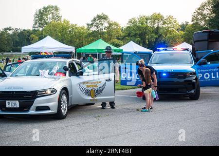 Child aged 7 interacting with State Trooper police officer at a community engagement event in BeaverCreek city, Ohio, USA Stock Photo