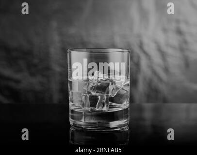 Black and white image of  whisky tumbler glass with spirits and ice in it shot with a moody feel. Stock Photo