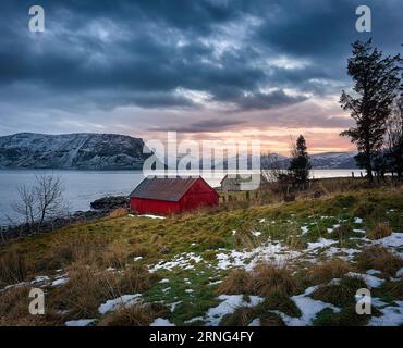 Beautiful sunrise with old fishing cabins and snowy mountain tops on Godøy, Ålesund, Norway Stock Photo