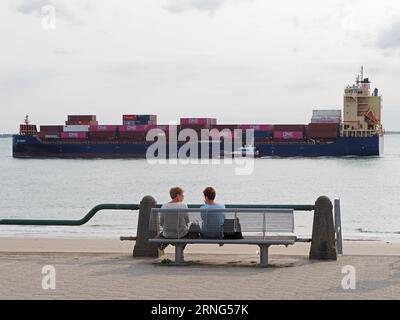 In the seaside city of Vlissingen, Zeeland, the Netherlands, the shipping lane is extremely close to the boulevard. Two ladies chatting on a summer ev Stock Photo