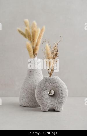 Decorative lava stone vases with dry flowers on light background Stock Photo
