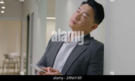 Sad upset tired middle-aged Asian man hold smartphone ethnic chinese japanese anxious desperate korean businessman employer manager mobile phone Stock Photo