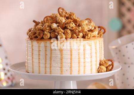 Caramel drip cake decorated with popcorn and pretzels against blurred background, closeup Stock Photo