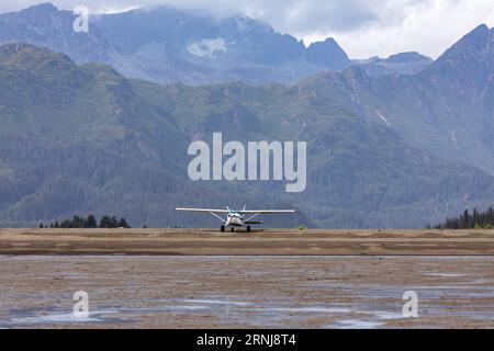 Small airplane in wilderness landed by bush pilot on gravel beach beneath mountains and glaciers Stock Photo