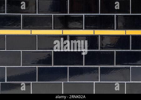 Black and indigo-colored ceramic subway tiled wall with horizontal yellow accent stripe. Stock Photo
