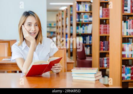 Asian university teen student portrait happy smile in campus library reading a book for self learning education. Stock Photo