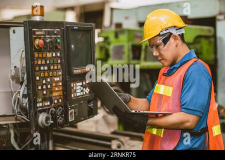 Engineer worker check service panel program operate CNC lathe machine with laptop computer fix repair old machine. Stock Photo