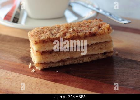 Slice of walnut layered cake bar, layers of sponge filled with jam and cream with walnut and egg white topping Stock Photo