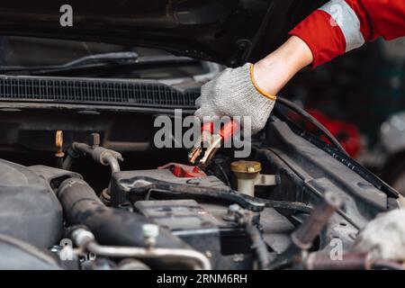 closeup mechanic male hand holding battery clamps grip for charging car battery in auto repair workshop Stock Photo