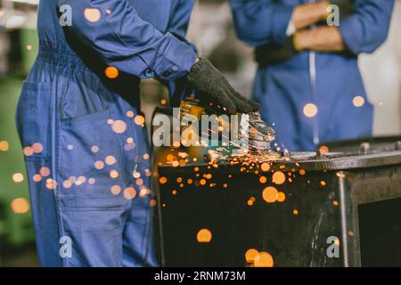Industrial Worker Using Angle Grinder and Cutting a Metal Sheet. Contractor in Safety Uniform and Hard Hat Manufacturing Metal Structures.Heavy Indust Stock Photo