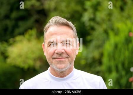 Close up Portrait of an attractive middle aged man in his fifties with a gentle smile while standing in the garden Stock Photo