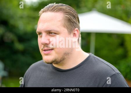 Young man in his twenties looks sideways in a friendly manner while standing in the garden Stock Photo