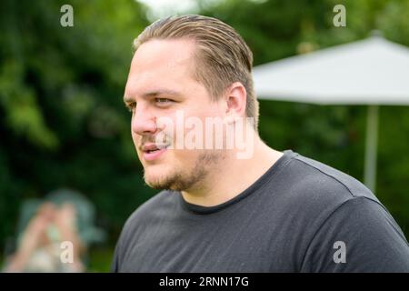 Young man in his twenties looks sideways in a friendly manner while standing in the garden Stock Photo