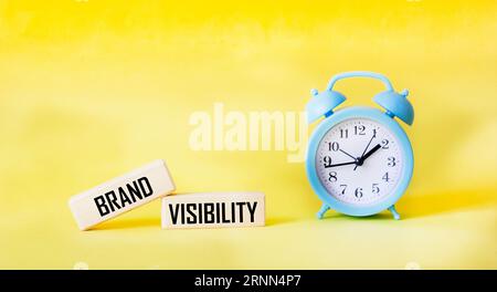 Brand visibility symbol. Wooden blocks with words.Yellow background with a clock. Copy space. Stock Photo