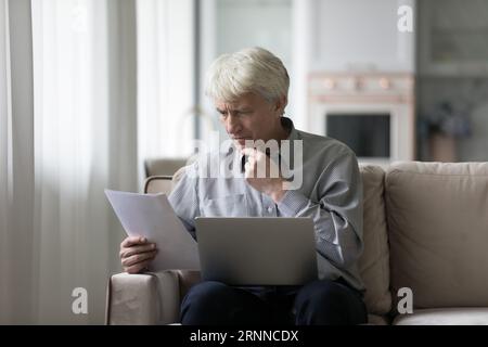 Serious concerned senior retired man reading document at home Stock Photo