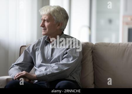 Serious concerned old retired man sitting on home sofa Stock Photo