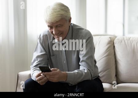 Positive focused senior pensioner man using smartphone at home Stock Photo