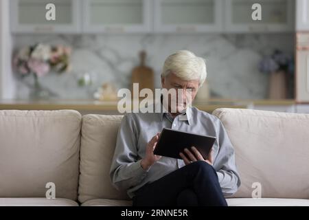 Serious Caucasian older retired man using tablet computer Stock Photo