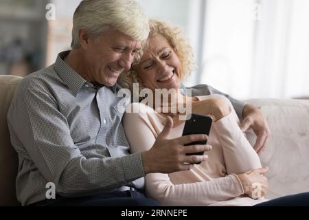 Cheerful mature elder couple using mobile phone at home Stock Photo
