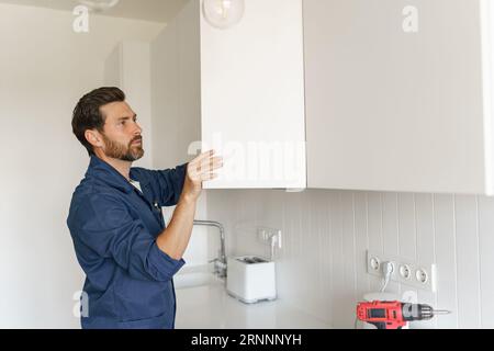 Professional male worker in uniform is repairing door of cabinet in kitchen. Home renovation concept Stock Photo