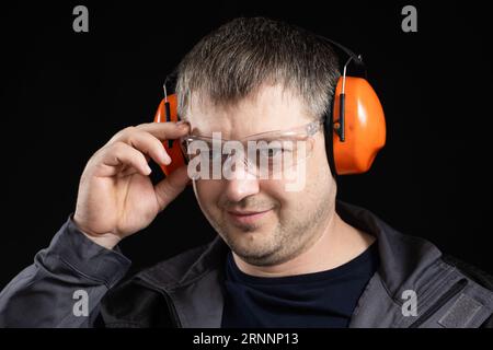 A man in earmuffs, glasses and overalls on a black background. Stock Photo