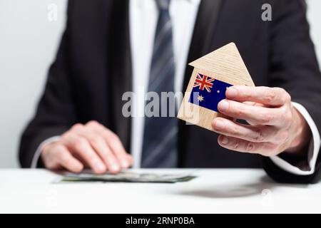 Businessman hand holding wooden home model with Australian flag. insurance and property concepts Stock Photo