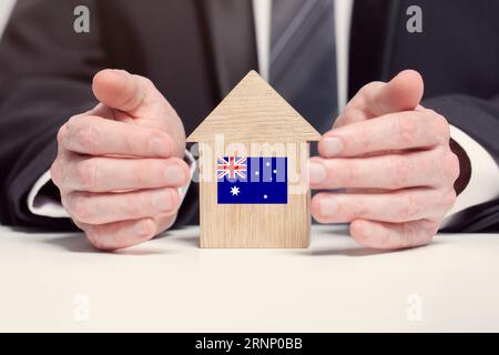 Businessman hand holding wooden home model with Australian flag. insurance and property concepts Stock Photo