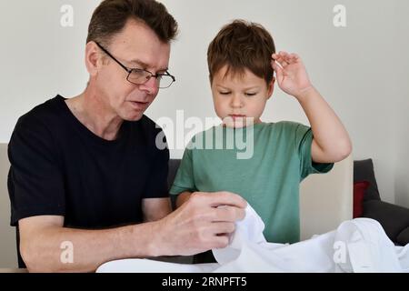 Father teaching his son how to sew on a button. Shot at home Stock Photo
