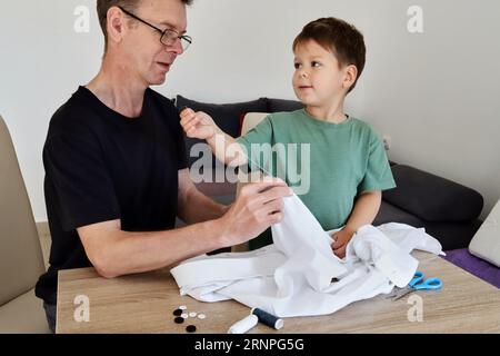 Father teaching his son how to sew on a button. Shot at home Stock Photo