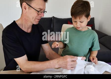 Father teaching his son how to sew on a button. Shot at home Stock Photo