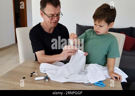 Father teaching his son how to sew on a button. Shot at home Stock Photo