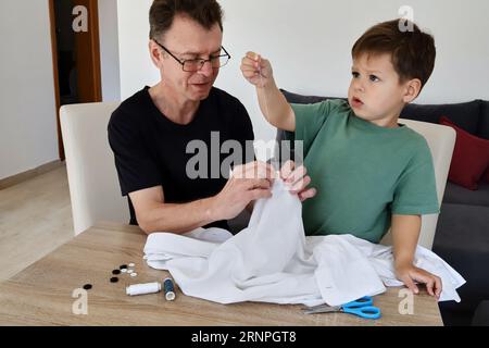 Father teaching his son how to sew on a button. Shot at home Stock Photo