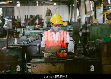Asian woman worker working in heavy metal industry workshop wearing facemask for hygiene healthy safety Stock Photo