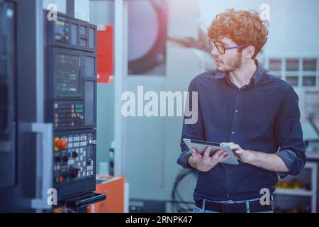 Professional young engineer factory worker programming CNC milling machine with a tablet computer. Stock Photo